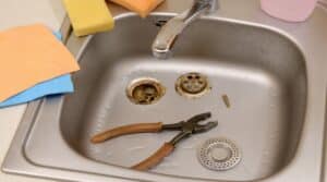 Pliers inside the silvery kitchen sink with a disassembled protective filter